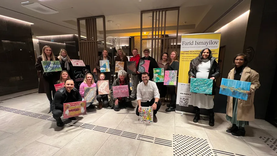 Group holding paintings, standing and kneeling indoors.