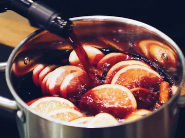 Cookware cooks red wine with orange slices and cinnamon sticks.