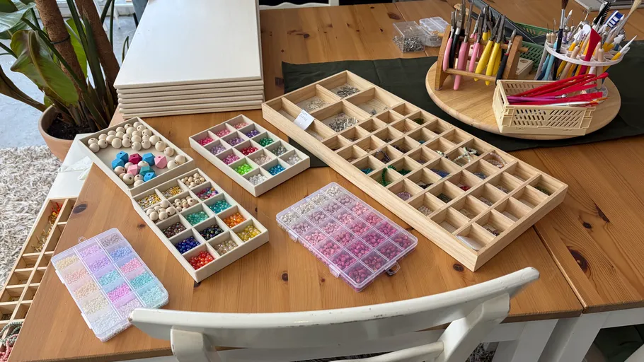 Bead assortment on wooden table, crafting tools present.