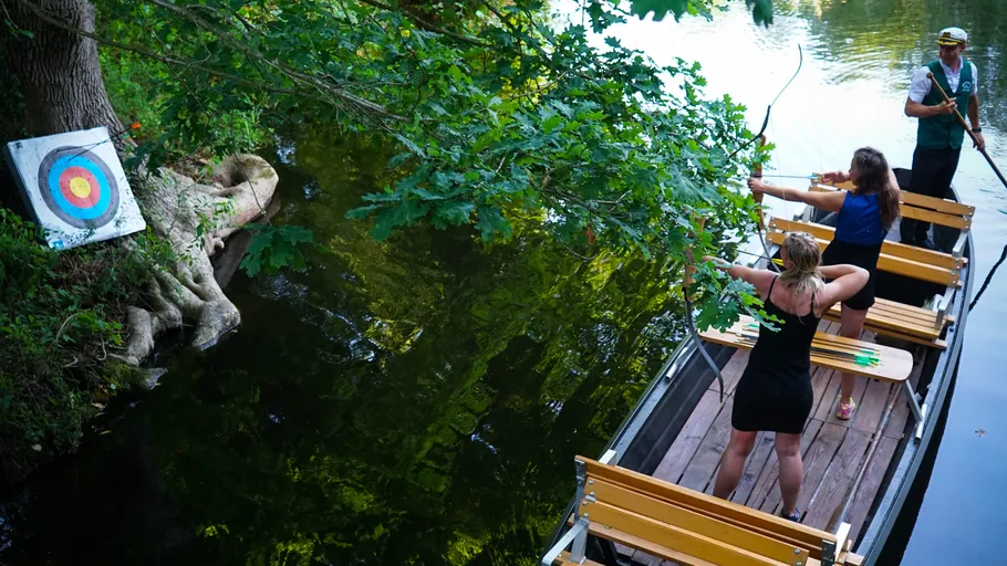 Menschen schießen Pfeile von einem Boot auf Zielscheibe.