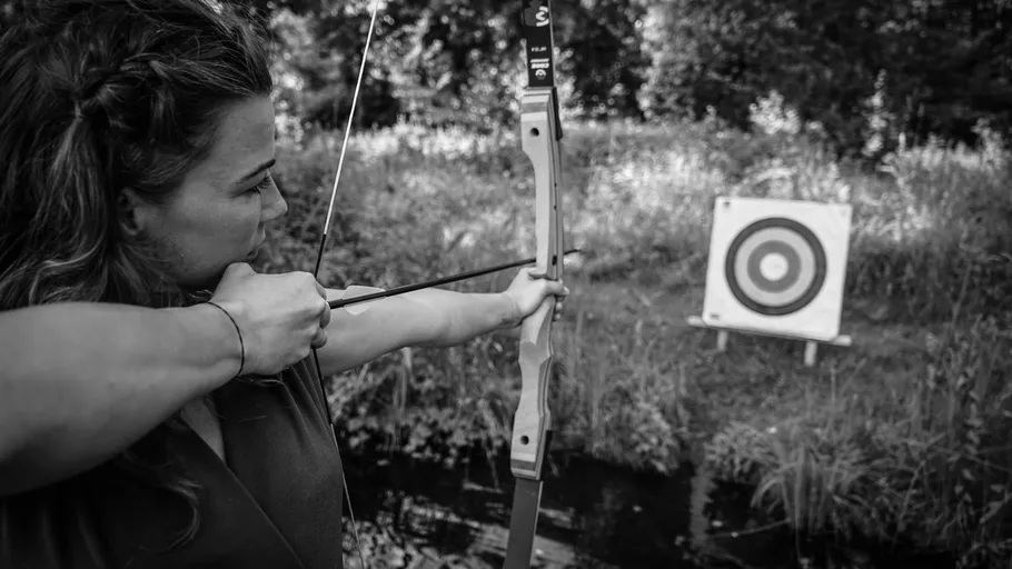 Woman aiming bow at target in forest.