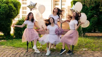 Four women in tutus pose with balloons outdoors.