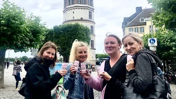 Vier Frauen halten Getränke, im Freien.