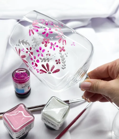 Handbemaltes Glas mit Blumenmotiv auf Tisch.