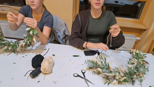 Two people crafting wreaths indoors with tools.