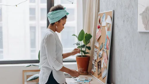Woman arranging items on corkboard in room.