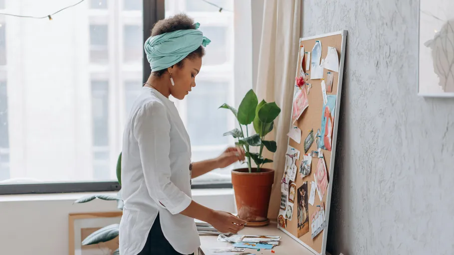 Woman arranging items on corkboard in room.
