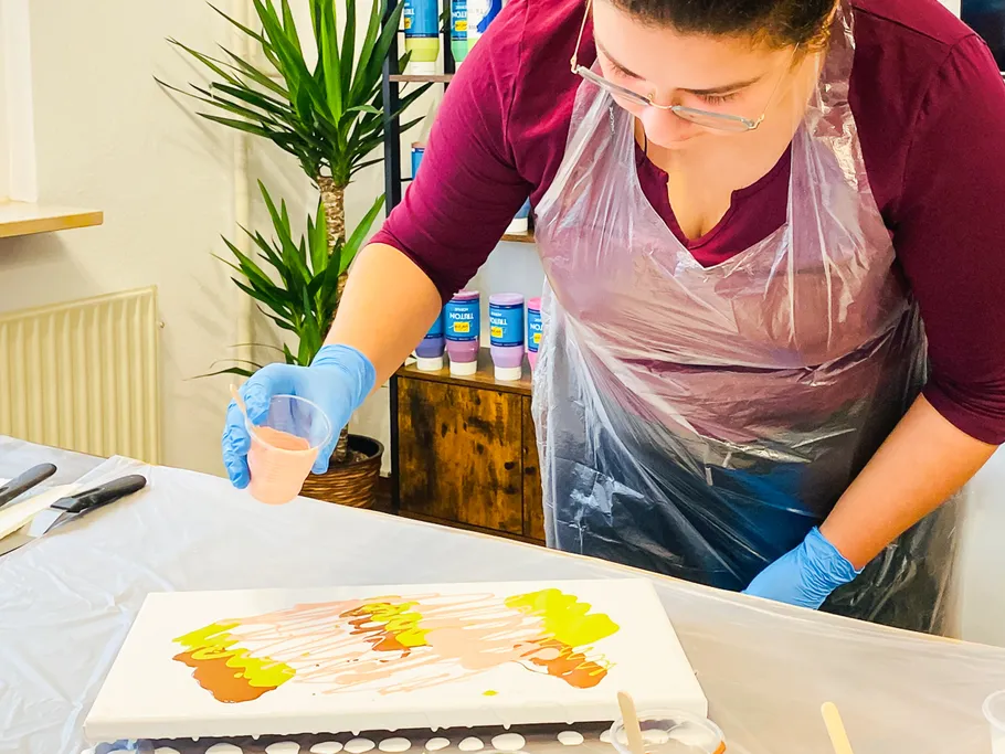 Woman pours paint on canvas in studio.