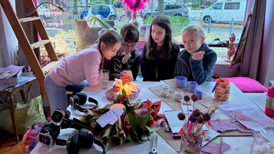 Kinder sitzen am Tisch und schauen auf ein Handy.