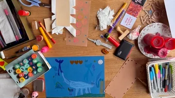 Bastelmaterialien und Kunstwerk auf Holztisch.