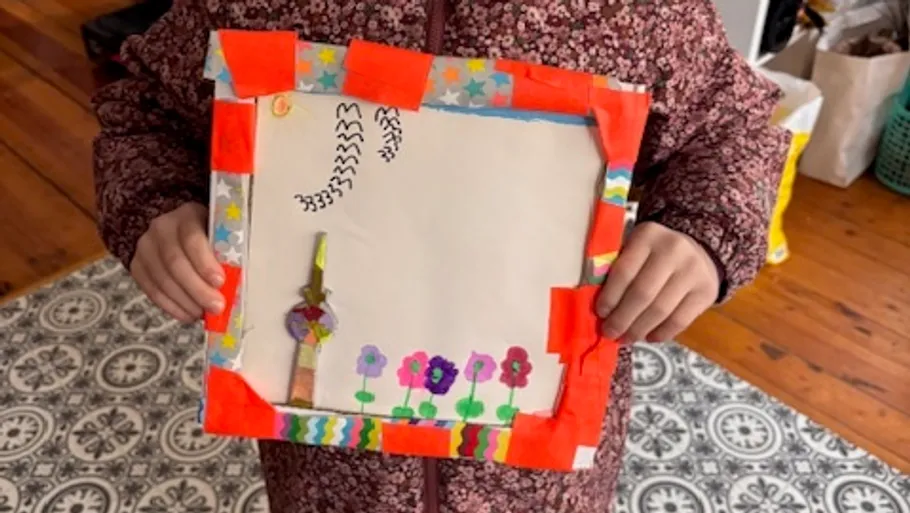Child holds colorful framed drawing.