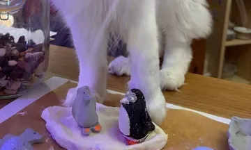 Cat near clay penguins on wooden table.