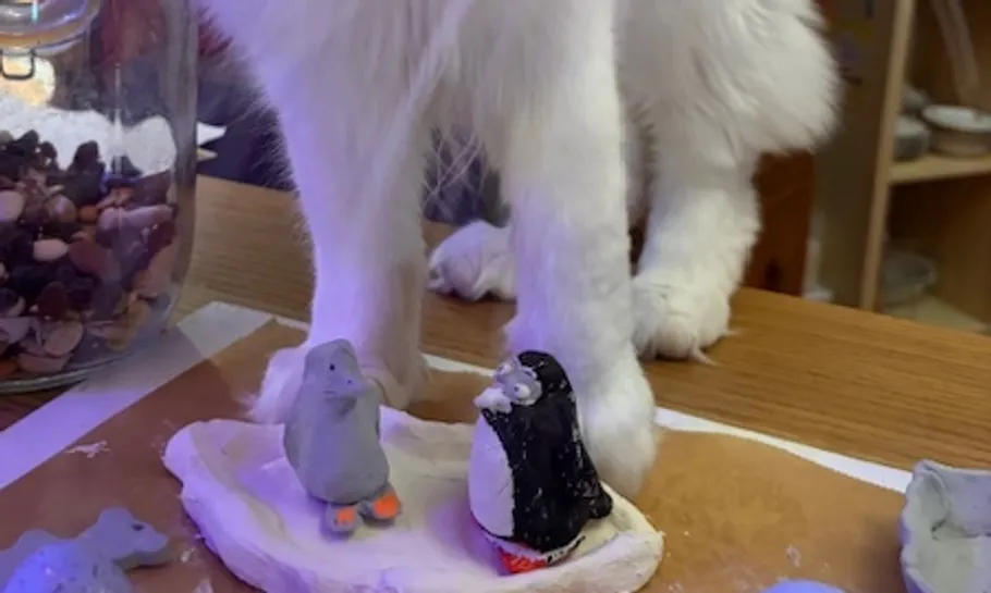 Katze neben Tonpinguinen auf Holztisch.