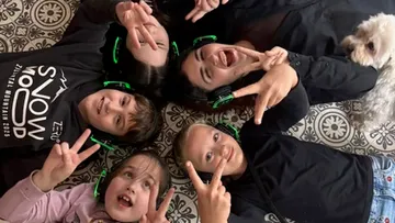 Kinder liegen auf dem Boden, tragen Kopfhörer, lächeln.
