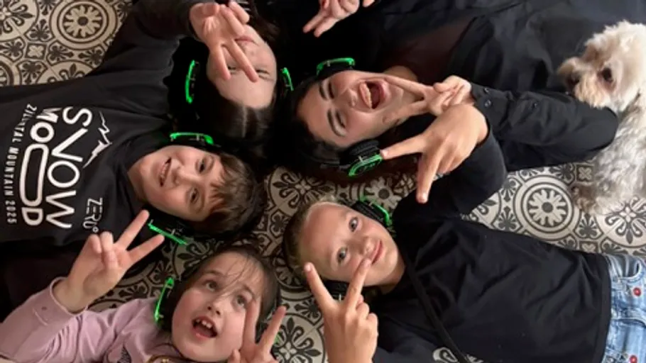 Children lying on floor wearing headphones, smiling.