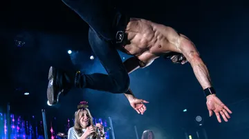 Shirtless man performing a flip on stage.