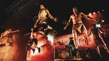 Performers leaping on stage with dramatic lighting.