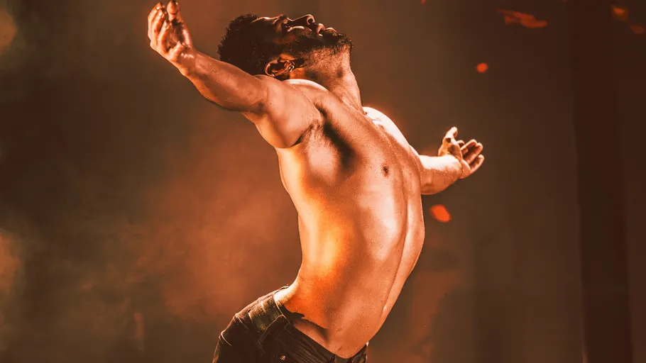 Shirtless man dancing in dramatic lighting.