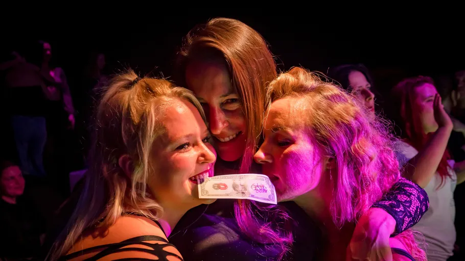 Drei Frauen lächeln mit einem Geldschein.