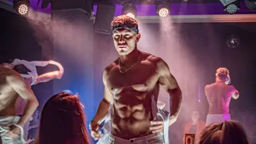 Shirtless man dancing on stage in nightclub.