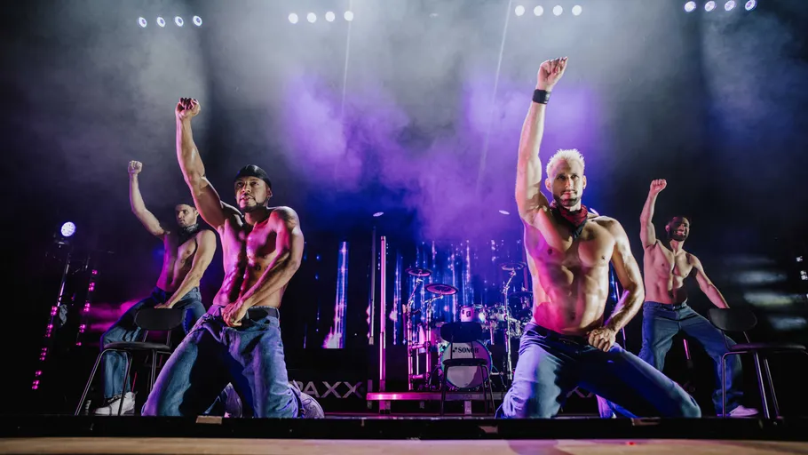 Four men performing shirtless on stage with lights.