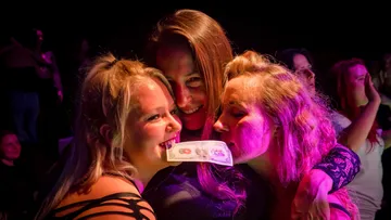 Drei Frauen lächeln, eine hält Geldschein.