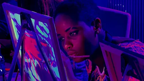 Person painting intensely under neon lights.