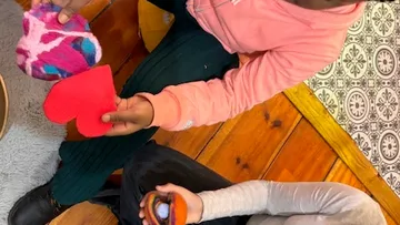 Children holding colorful heart-shaped objects indoors.