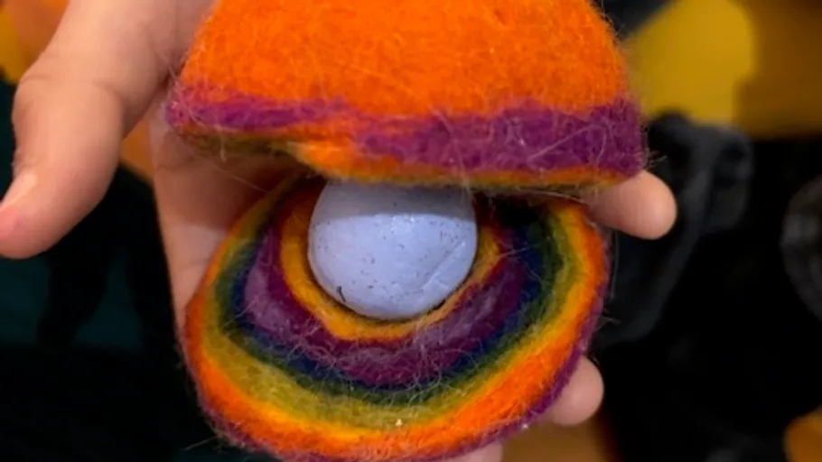 Hand holds colorful wool clam with pearl.