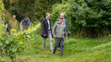 Group of men walking on grassy path surrounded by trees.