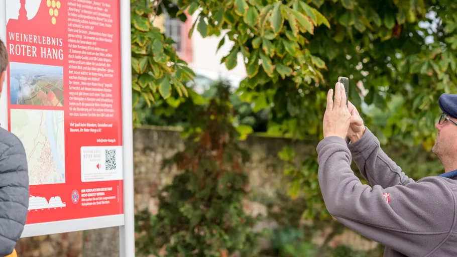 Man photographing sign about wine experience outdoors.