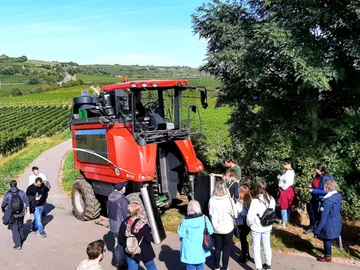 A full harvester is standing on a path surrounded by people.