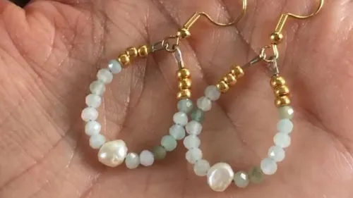 Hand holding beaded earrings with gold accents.