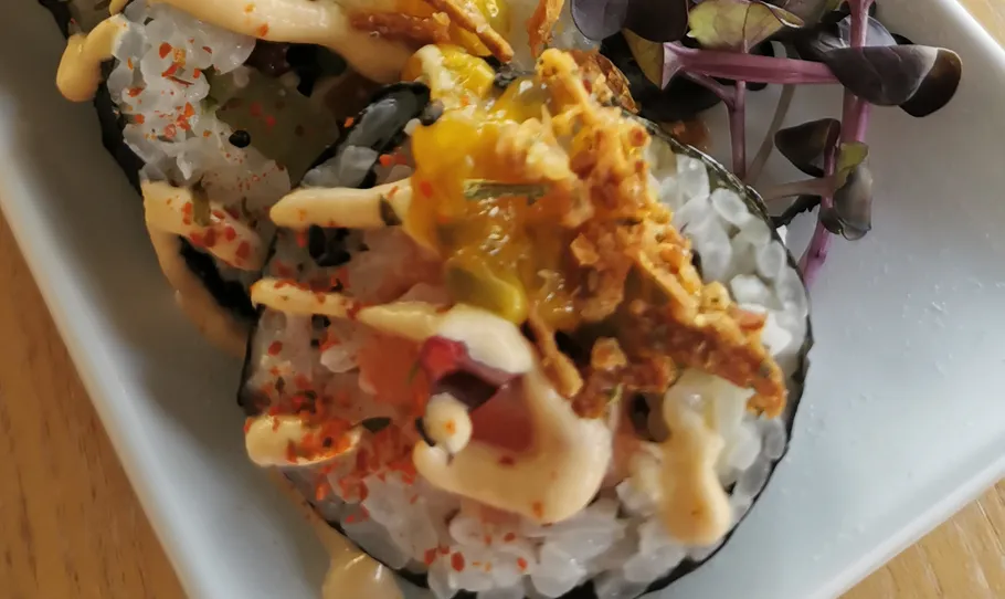 Sushi-Rolle mit Belag auf weißem Teller.
