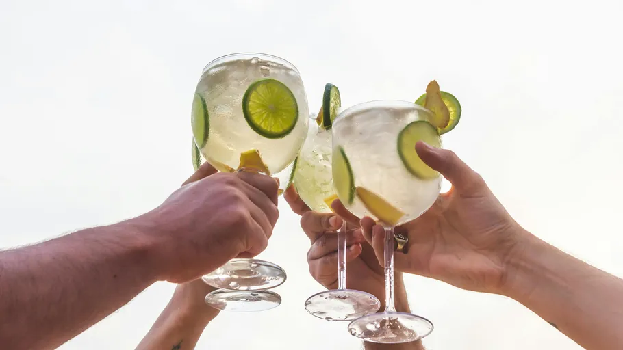 Hands clinking glasses with drinks, outdoor setting.