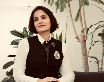 Woman sitting, wearing formal attire, indoor plants.