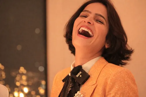 Lachende Frau in goldenem Blazer drinnen.