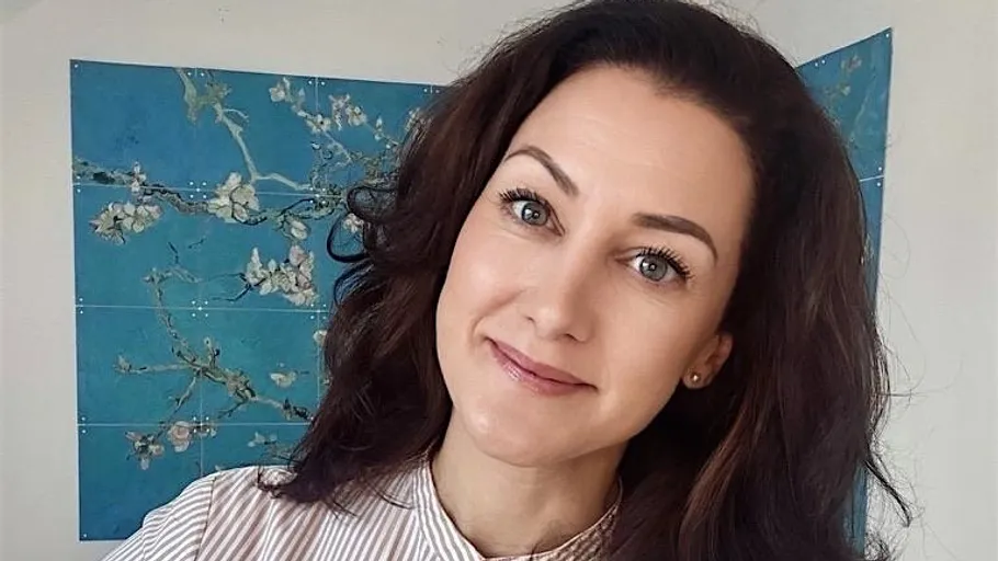 Lächelnde Frau mit Blumenbild dahinter.