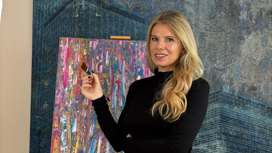 Woman holding brush, standing by colorful painting.