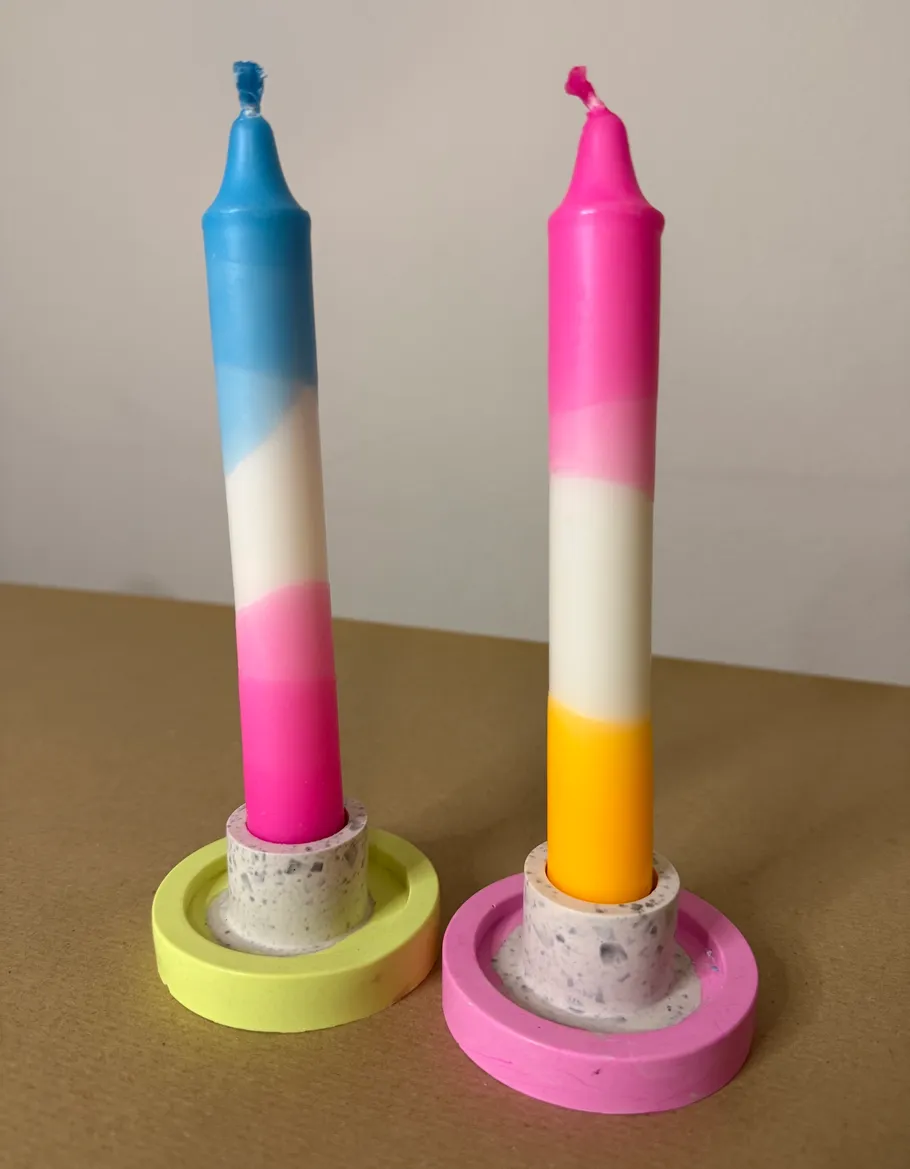 Zwei bunte Kerzen mit einzigartigen Haltern auf Tisch.