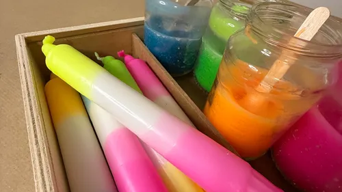 Bunte Kerzen und Gläser mit farbigem Wachs.