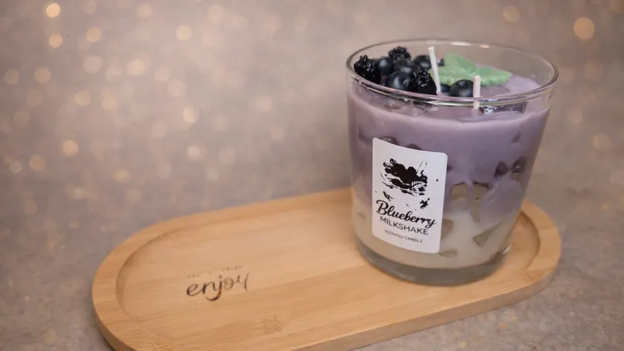 Lila Kerze im Glas mit Blaubeer-Dekoration.