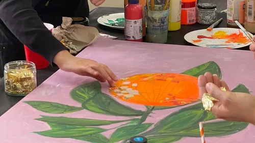 Hands decorating painting with gold leaf.