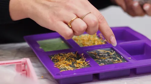 Hand placing ingredients in soap mold tray.