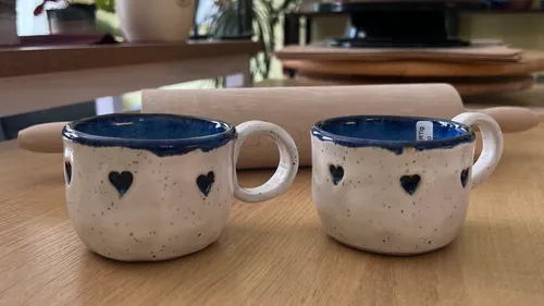 Two ceramic mugs with heart designs on table.