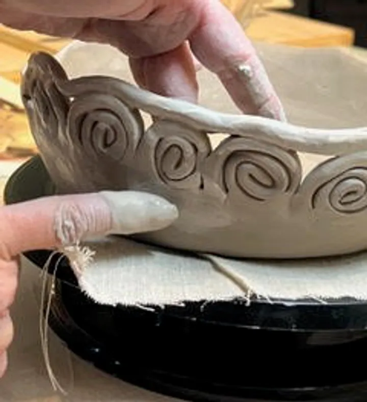 Hands shaping clay bowl with spiral design.