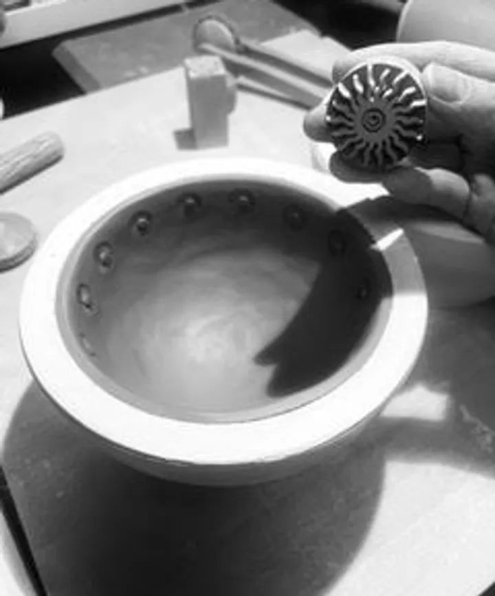 Hand holding stamp over ceramic bowl.