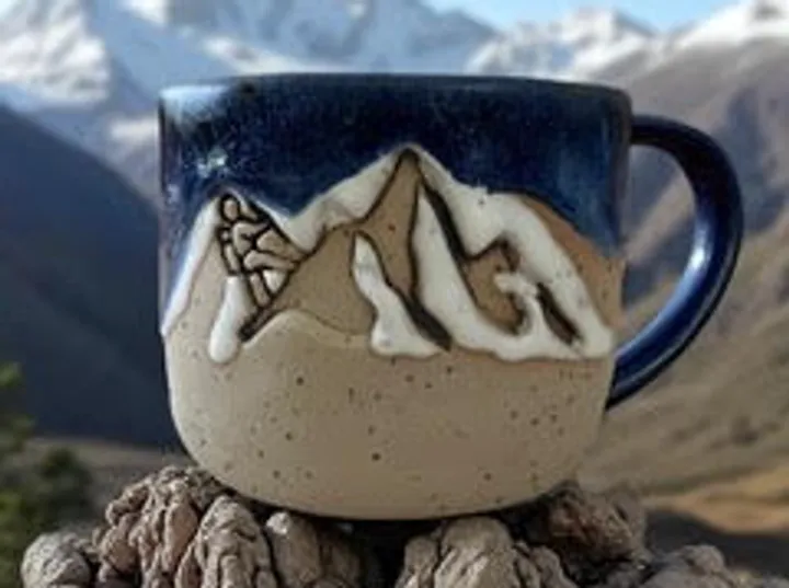 Ceramic mug with mountain design outdoors.