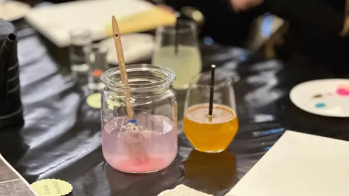 Paintbrush in jar, drinks on table, art supplies.
