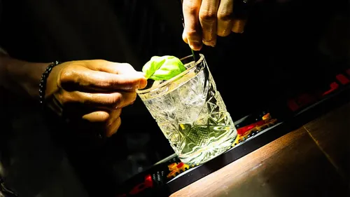 Hände garnieren Cocktail mit Basilikumblättern.